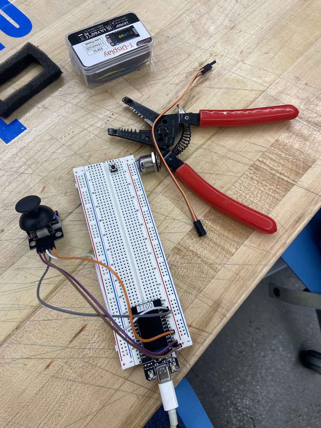 ESP-32 attached to the breadboard with wires sticking out of it attaching to the joystick on a brown table next to a pair of red wirecutters.