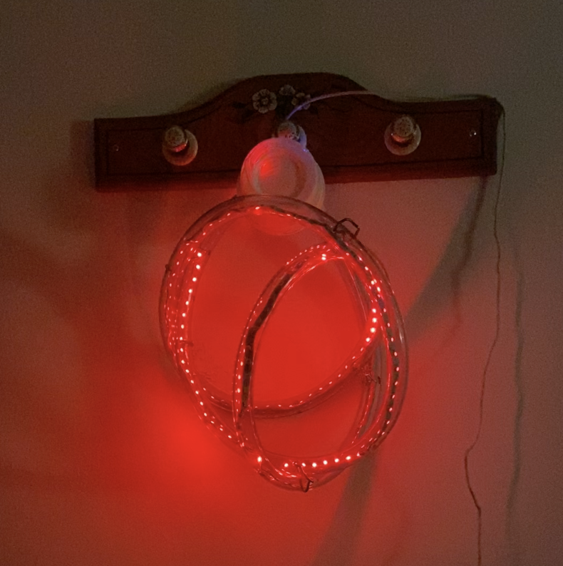 The disco ball hung up, flashing red. It is attached to a wooden coat hook mounted to a wall.